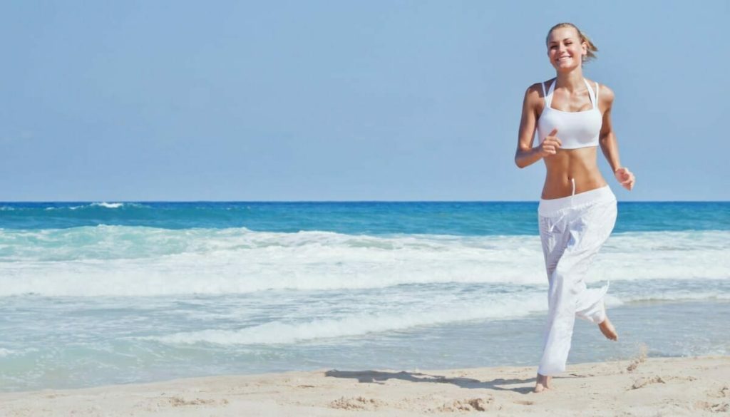 Frau in weißer Kleidung, die über den Strand joggt